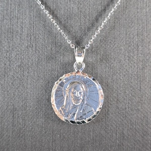 May include: Silver chain necklace with a round pendant featuring a detailed image of a person's face.