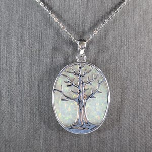May include: A silver chain necklace with a silver oval pendant featuring a tree of life design with an iridescent opal inlay.