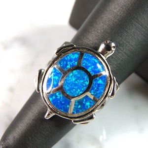 May include: A silver ring with a blue opal turtle design.