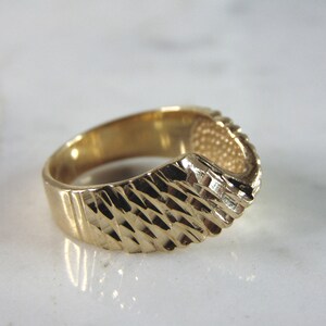 May include: A gold ring with a textured, diamond-shaped pattern. The ring is open on one side, creating a unique design.