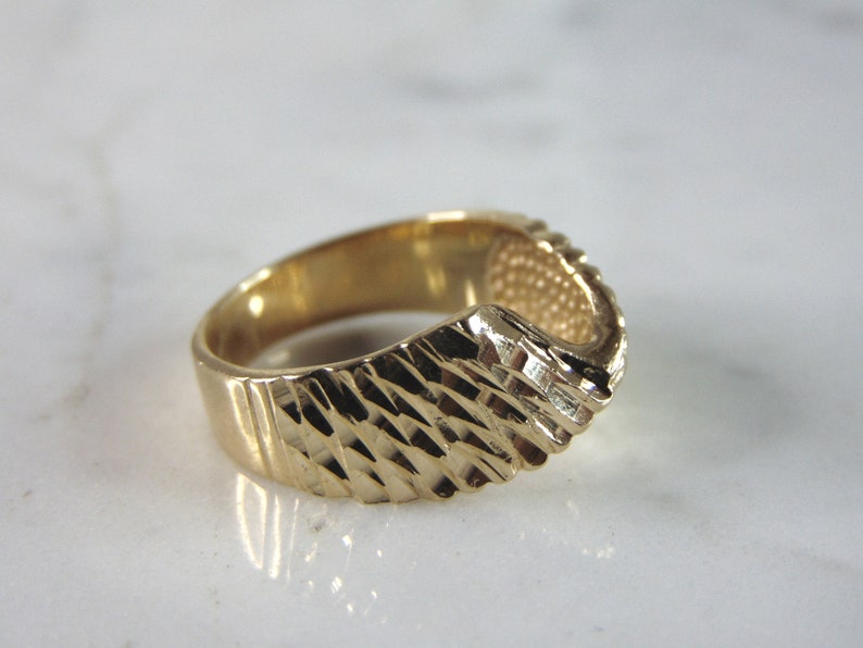 May include: A gold ring with a textured, diamond-shaped pattern. The ring is open on one side, creating a unique design.