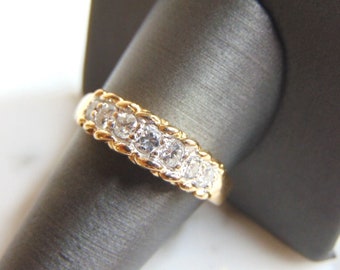 Puede incluir: Un anillo de banda de oro con una fila de diamantes redondos transparentes engastados en un diseño trenzado.