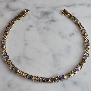 May include: A gold chain bracelet with a delicate design and purple gemstones.