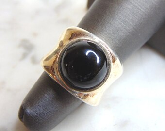 May include: A silver ring with a black gemstone set in a square-shaped bezel. The ring has a unique, modern design.