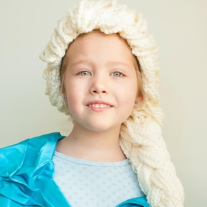 Könnte beinhalten: Ein junges Mädchen trägt eine cremefarbene, gestrickte Perücke mit einem langen Zopf und ein hellblaues Satin-Kostüm. Die Perücke ist so gestylt, dass sie der Frisur einer Figur ähnelt. Das Kostüm hat ein hellblaues Oberteil darunter.