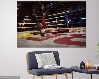 May include: A boxer lies on the mat in a boxing ring, defeated. A referee stands over him, looking down. The ring is surrounded by spectators.