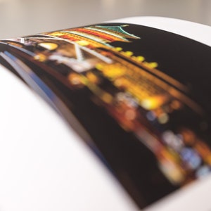 May include: A photograph of a building at night, with a focus on the colorful lights and architectural details. The image is slightly blurred, creating a soft, dreamlike effect. The photograph is on a white page.