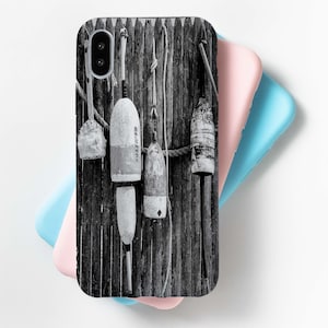 May include: Black and white photo of a wooden fence with four buoys hanging from it. The buoys are made of wood and have a rope attached to them. The buoys are all different shapes and sizes. The photo is in a vintage style.