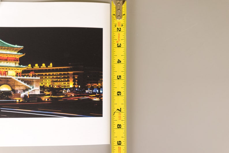 May include: A photograph of a nighttime cityscape with a yellow measuring tape. The cityscape features a building with a green roof and yellow lights. The measuring tape shows a measurement of approximately 8 inches.