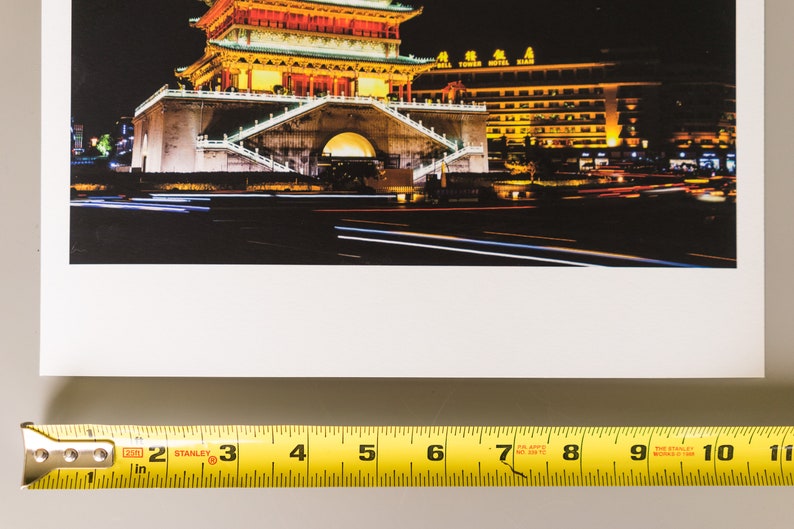 May include: A photograph of a Chinese pagoda at night, illuminated with warm yellow and orange lights. The image captures the building's intricate architecture and the surrounding cityscape, with streaks of light from passing vehicles.