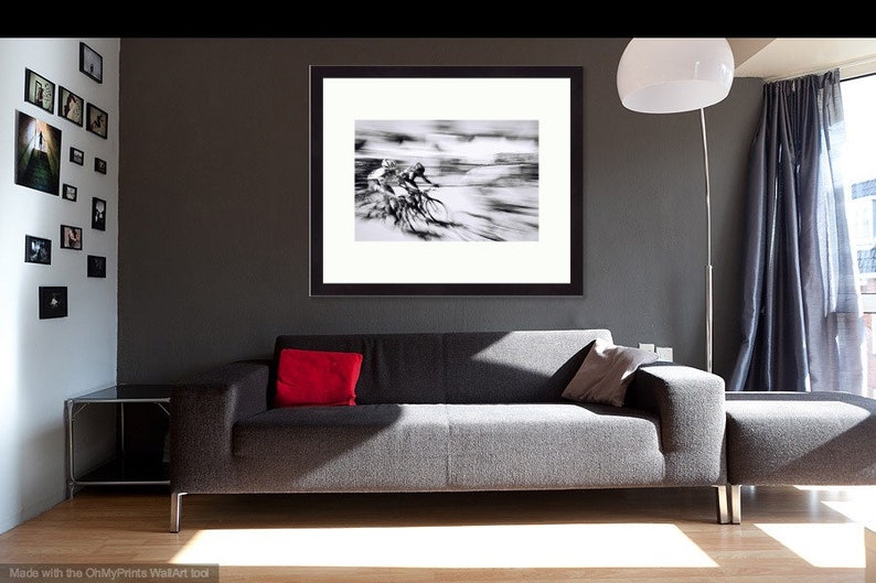 May include: Black and white framed print of cyclists in motion, displayed above a gray sofa with a red pillow. The room features a modern design with a floor lamp and a gallery wall of framed photos.