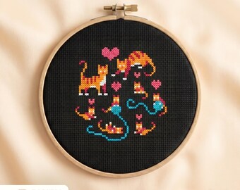 May include: A cross-stitch embroidery hoop featuring a black fabric with a pattern of orange and yellow cats, pink hearts, and blue yarn. The wooden hoop holds the stitched design. The words "DIGITAL DOWNLOAD" are printed on the lower left.