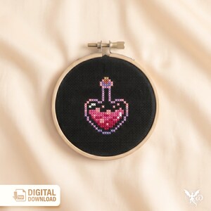 May include: A cross-stitch design of a potion bottle in a wooden embroidery hoop. The bottle is pink and purple on a black background. The text "DIGITAL DOWNLOAD" is in the lower left corner.