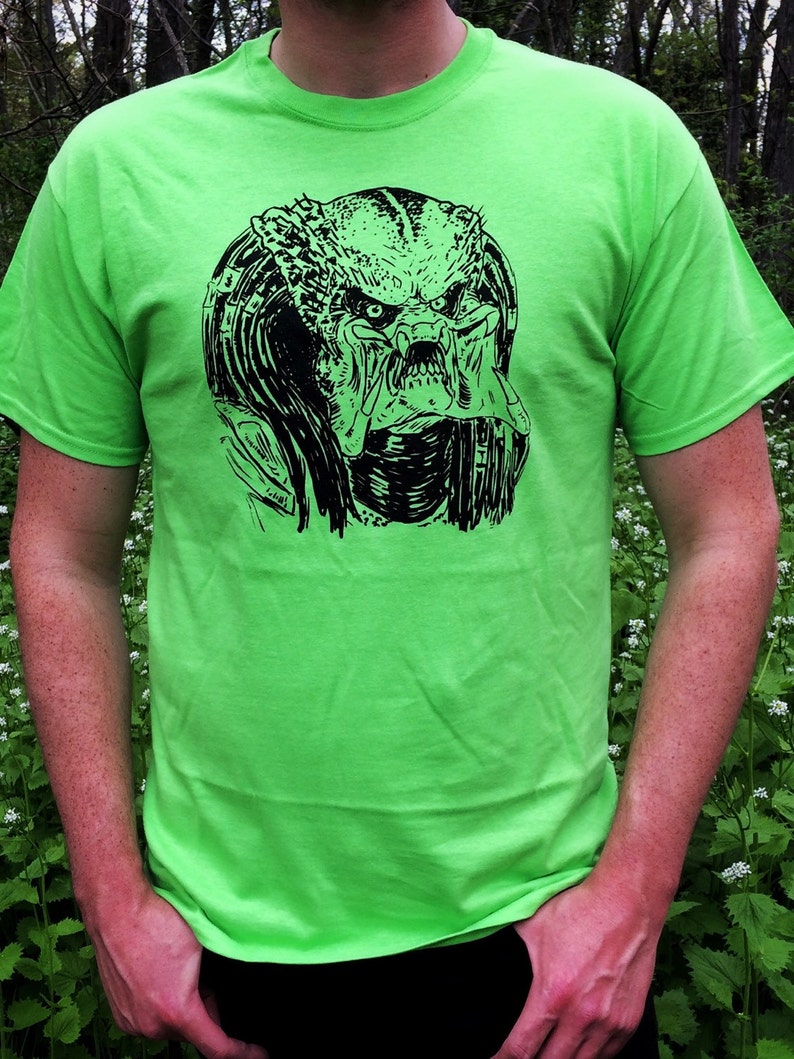 May include: A neon green t-shirt with a black and white graphic print of a Predator's head.