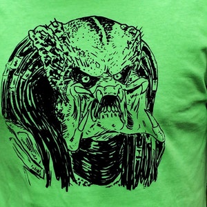May include: A black and white graphic print of a Predator's head on a bright green t-shirt.