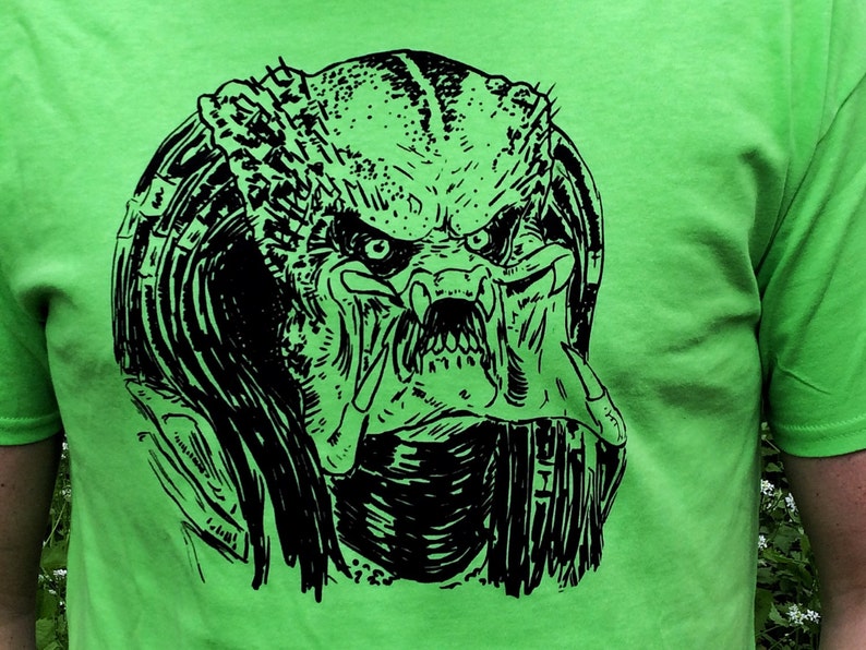 May include: A black and white graphic print of a Predator's head on a bright green t-shirt.