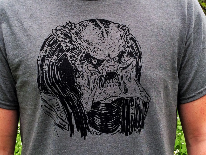 May include: A black and white graphic print of a Predator's head on a gray t-shirt.