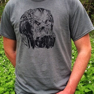 May include: A gray t-shirt with a black and white graphic print of the Predator's face.