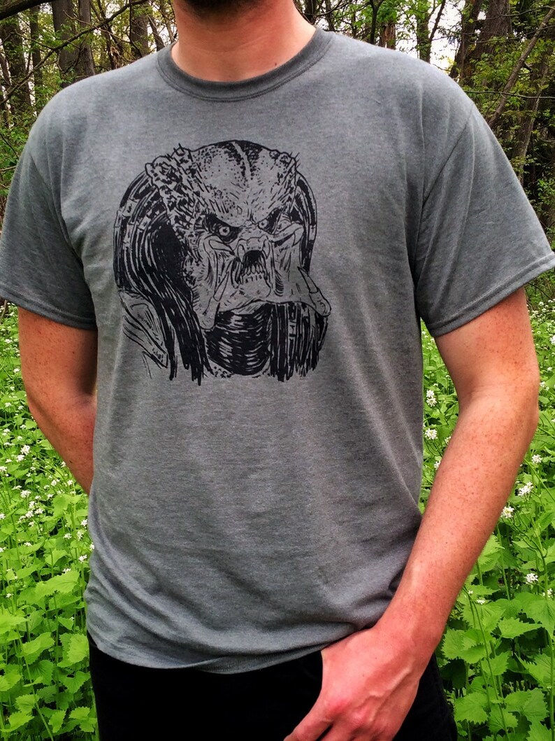 May include: A gray t-shirt with a black and white graphic print of the Predator's face.