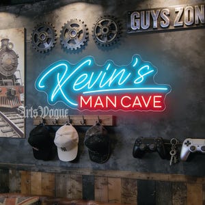 Peut inclure: Une décoration murale comprenant une enseigne néon affichant Kevin's MAN CAVE en bleu et rouge, une plaque métallique GUYS ZONE, trois engrenages décoratifs, une affiche de train, un porte-manteau avec trois casquettes et deux manettes de jeu.