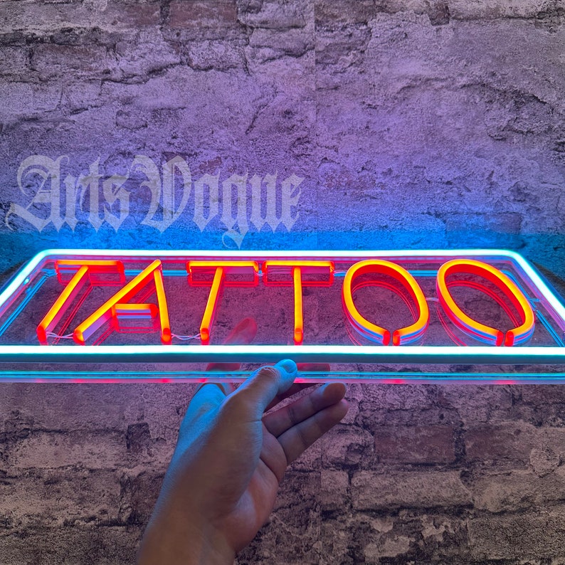 May include: A neon sign with the word "TATTOO" in red neon letters on a clear glass background. The sign is mounted on a brick wall.