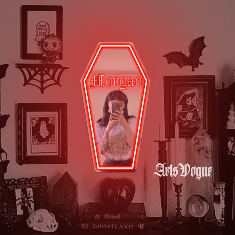 May include: A red neon sign in the shape of a coffin with the name "Morgan" written in gothic font. The sign is hanging on a wall with a dark background. The sign is surrounded by various gothic decor, including a spiderweb, a bat, and a skull.