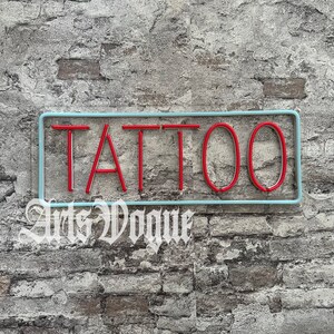 May include: A blue and white neon sign with the word "TATTOO" in red neon letters against a brick wall background.