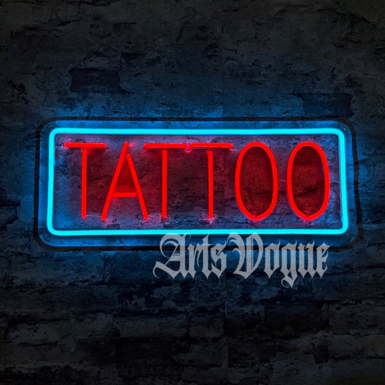 May include: A neon sign with a blue border and red letters that reads "TATTOO". The sign is mounted on a brick wall. The text "Arts Vogue" is written below the sign.