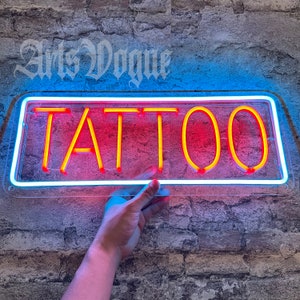 May include: A neon sign with a white border and a red background. The sign says "TATTOO" in yellow letters.
