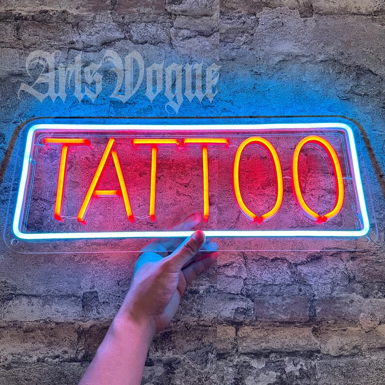 May include: A neon sign with a white border and a red background. The sign says "TATTOO" in yellow letters.