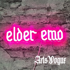Könnte beinhalten: Ein pinkfarbenes Neon-Schild mit den Worten "elder emo" in weißen Buchstaben vor einem Hintergrund aus Backsteinmauer. Die Worte "Arts Vogue" sind in weiß unter dem Schild geschrieben.