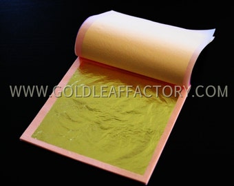 May include: A sheet of gold leaf, folded in half, with a pink paper backing. The gold leaf is a bright, shiny yellow color. The text "www.goldleaffactory.com" is printed on the pink paper.