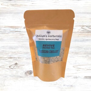 May include: A brown paper pouch with a clear window showing a blend of dried herbs. The pouch has a label that reads "Yuliya's Naturals Holistic Apothecary Shop REVIVE Herbal Tea for energy, vigor, and emotional calmness."