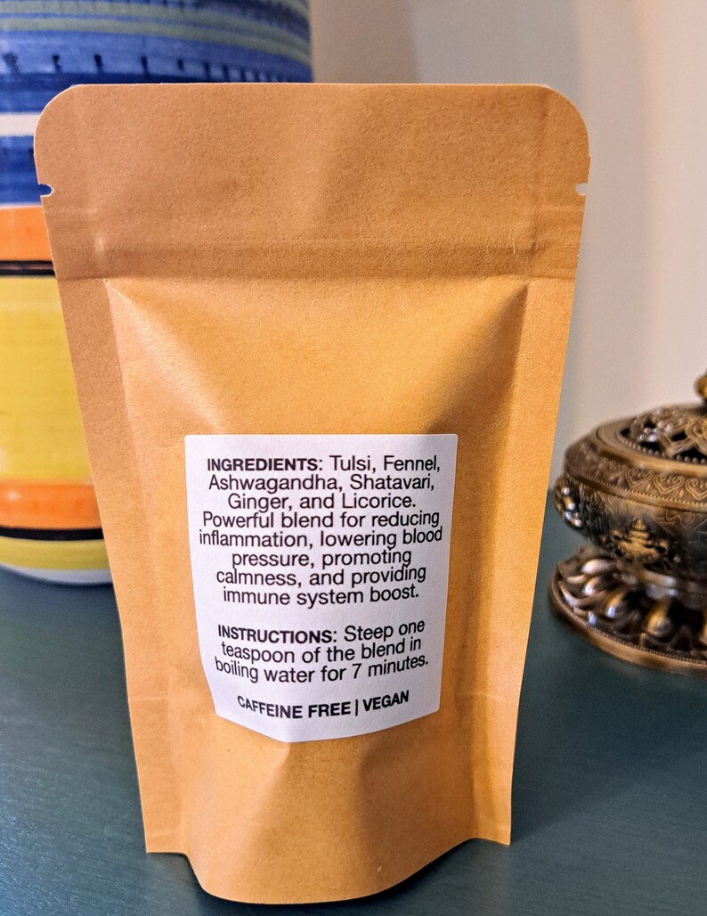 May include: A brown paper pouch with a white label listing the ingredients and instructions for a caffeine-free, vegan herbal tea blend. The ingredients include Tulsi, Fennel, Ashwagandha, Shatavari, Ginger, and Licorice. The instructions state to steep one teaspoon of the blend in boiling water for 7 minutes.