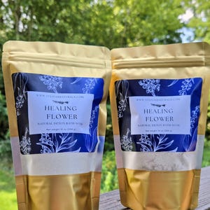 May include: Two gold and blue pouches of Healing Flower Natural Detox Bath Soak. The pouches have a blue and white floral design with the text "Healing Flower" and "Natural Detox Bath Soak". Each pouch contains 10 oz (284 g) of product.