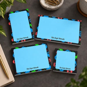 May include: Four rectangular sticky note pads of varying sizes with a light blue centre and a black border featuring colourful skull icons. Each pad displays the text No Safe Words in a black script font at the bottom of the light blue area.
