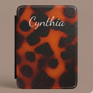 Op de afbeelding: Een rechthoekige hoes met een schildpadpatroon in bruin- en zwarttinten. De naam "Cynthia" staat in cursiefschrift op de voorkant. De hoes heeft een zwarte rug.