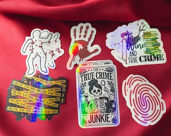 Puede incluir: Un conjunto de pegatinas holográficas con temas de crímenes reales. Las pegatinas incluyen una huella de mano, una huella dactilar, un diseño de cinta de la escena del crimen, un esqueleto con una lupa y un diseño con el texto "Wine and True Crime".