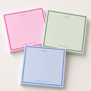 May include: Three square paper note pads in pastel pink, light green, and light blue. Each pad features a colored border, a centered monogram at the top, and a name printed at the bottom. The pink pad reads D|M and Dahlia Martinez, the green pad reads L|V and Lily Vargas, and the blue pad reads D|M and Dahlia Martinez.