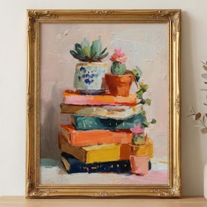 May include: An oil painting in a gold ornate frame depicts a stack of colorful books topped with potted succulents and a cactus. The books are in shades of blue, orange, and yellow. The painting has a textured, impressionistic style.