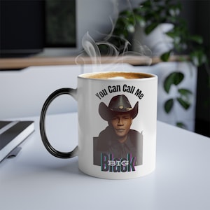 May include: White ceramic mug with a black handle. The mug features a black and white image of a man wearing a cowboy hat. The text "You Can Call Me Big Black" is printed on the mug.