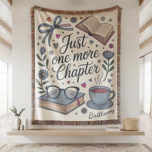 May include: Cream-colored throw blanket with the text "Just one more chapter" and illustrations of books, glasses, a teacup, and flowers. The blanket has a fringed edge and a bow design. The name "Brittany" is also on the blanket.