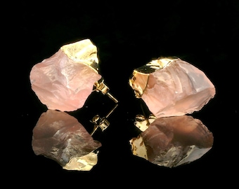 May include: A pair of rose quartz earrings with gold accents. The earrings are shaped like rough, natural crystals.