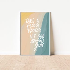 Puede incluir: Una impresión enmarcada en blanco con un fondo de acuarela en tonos amarillos, melocotón y azul. El texto "Take a fresh breath Let God renew you" está escrito en letras blancas cursivas.