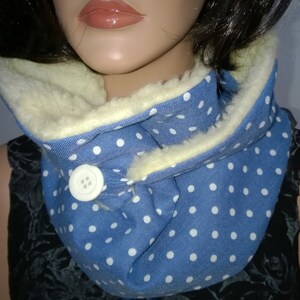 Puede incluir: Un calentador de cuello azul y blanco con lunares, con un bot&oacute;n blanco y un forro de vell&oacute;n crema.