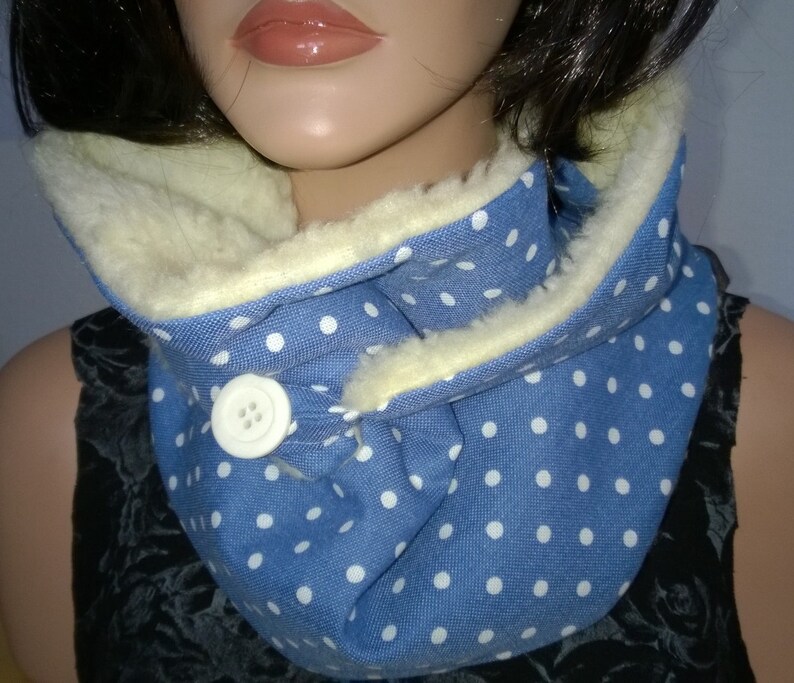 Puede incluir: Un calentador de cuello azul y blanco con lunares, con un bot&oacute;n blanco y un forro de vell&oacute;n crema.