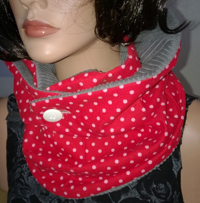 Puede incluir: Cuello de punto rojo con lunares blancos y forro de felpa gris. El cuello tiene un cierre de bot&oacute;n.