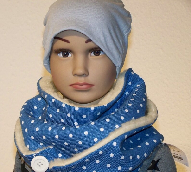 Puede incluir: Una bufanda azul y blanca con lunares, con forro de lana blanca y un bot&oacute;n blanco. La bufanda la lleva un ni&ntilde;o que lleva una boina azul claro.