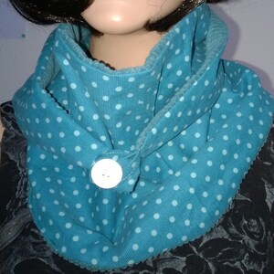 Puede incluir: Una bufanda de cuello de tortuga azul turquesa con lunares blancos y un bot&oacute;n blanco. La bufanda est&aacute; hecha de una tela suave y texturizada.