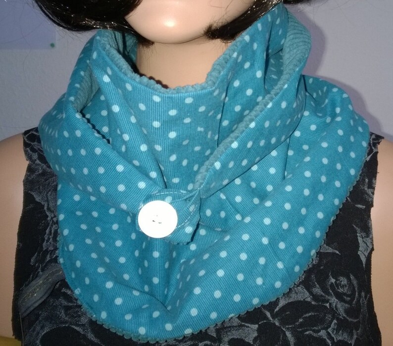 Puede incluir: Una bufanda de cuello de tortuga azul turquesa con lunares blancos y un bot&oacute;n blanco. La bufanda est&aacute; hecha de una tela suave y texturizada.